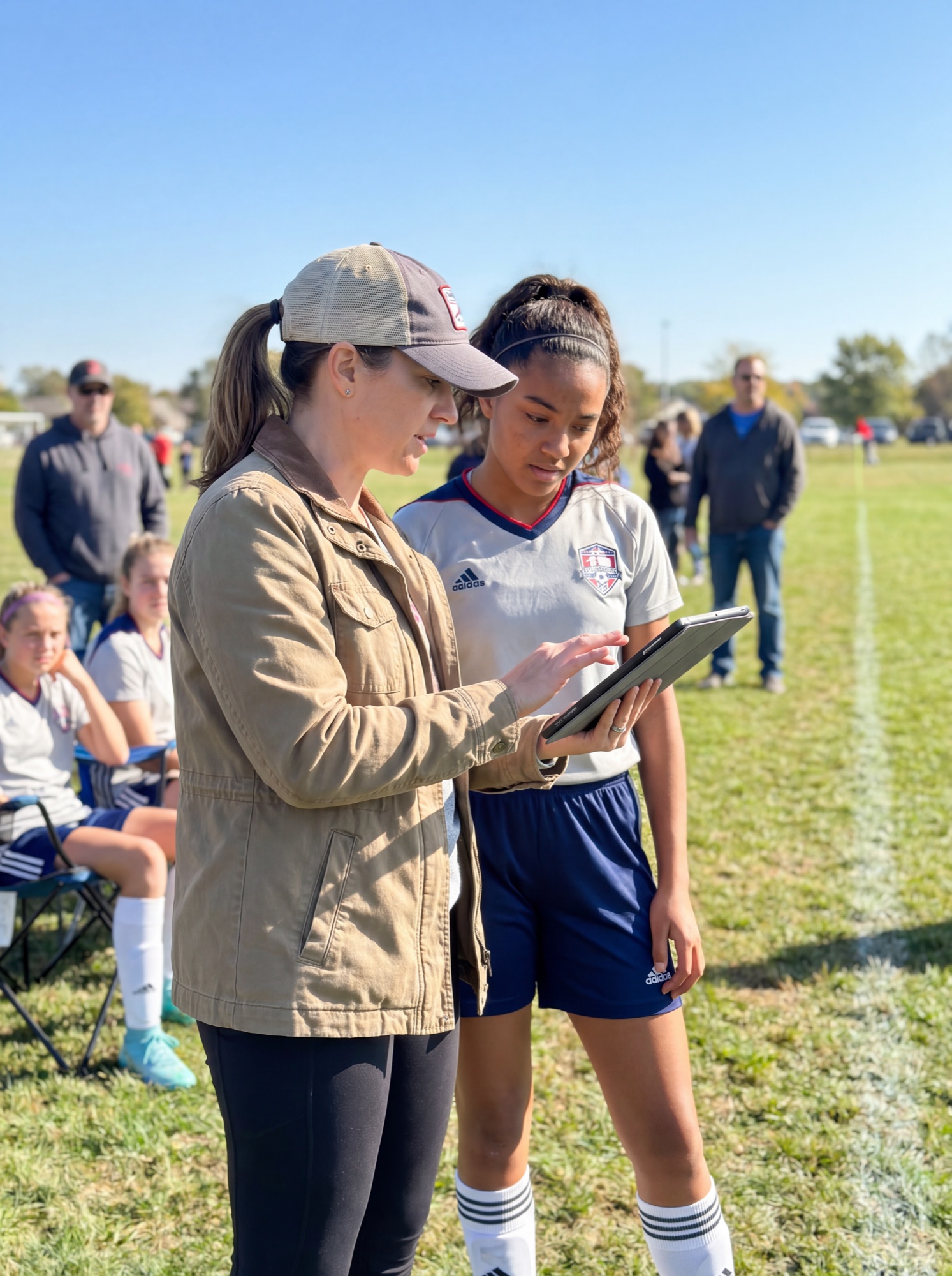 A soccer mom showing her daughter the game on a tablet on the sideline